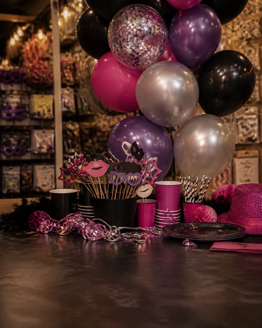 Mesa de despedida con globos fucsias, violetas y accesorios para fotos